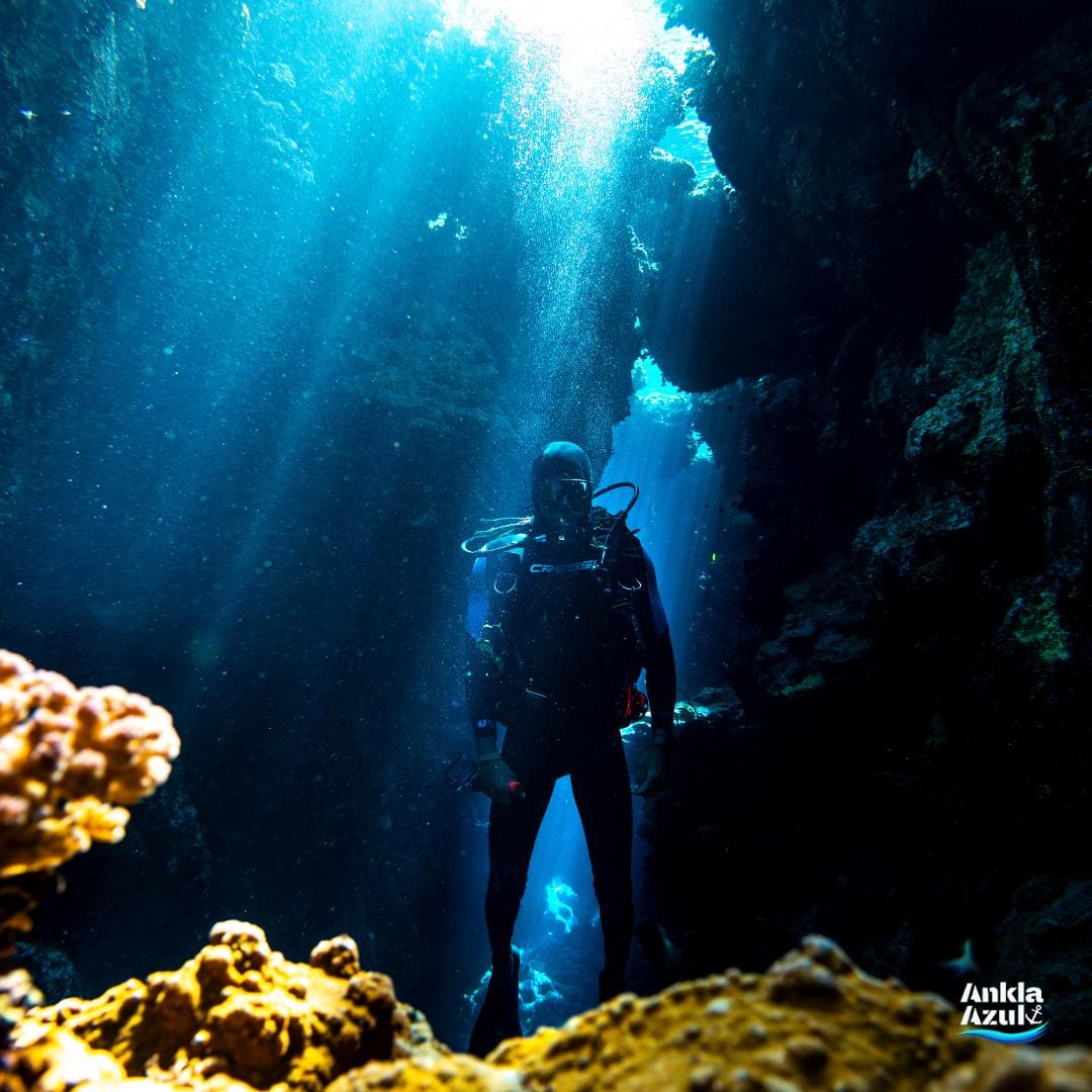 Diver standing in an underwater canyon with sunbeams filtering through, at Ankla Azul.