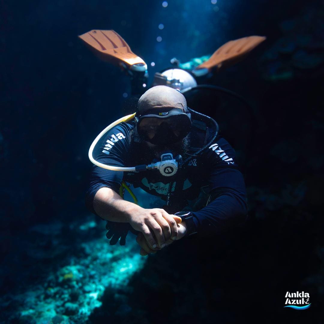 Scuba diver underwater in dark waters with orange fins and a white tank at Ankla Azul