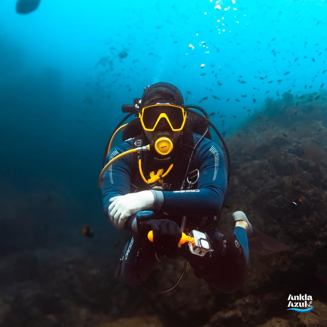 Scuba diver wearing a yellow mask posing underwater with a camera at Ankla Azul