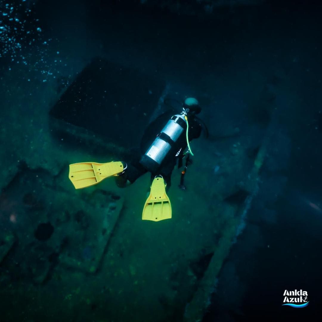 Scuba diver wearing a yellow mask posing underwater with a camera at Ankla Azul