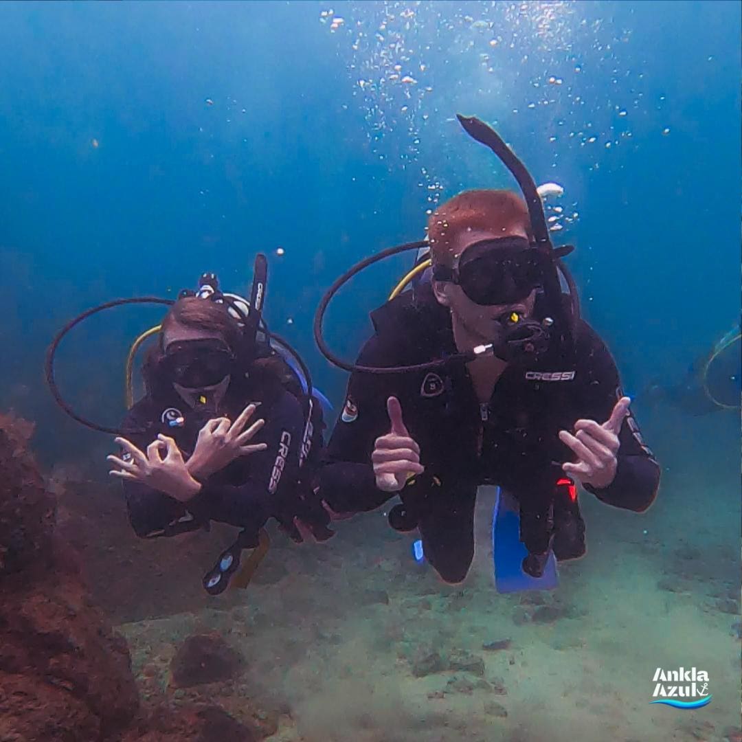 Two scuba students underwater making OK and ‘hang loose’ signals at Ankla Azul dive center.